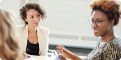 Three women in a meeting, one speaking, the others listening