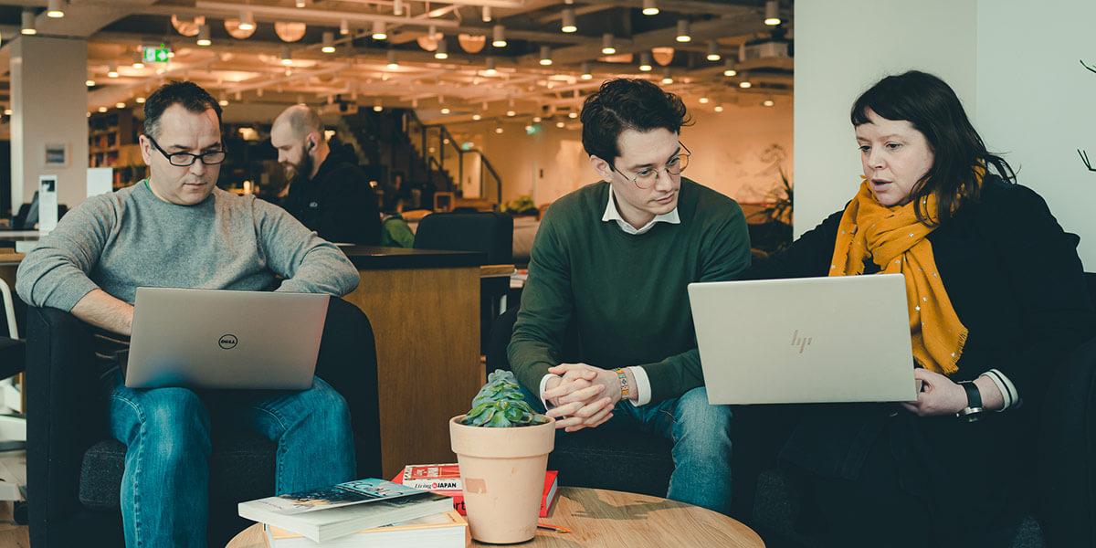 Three people sit round a coffee table, working on laptops